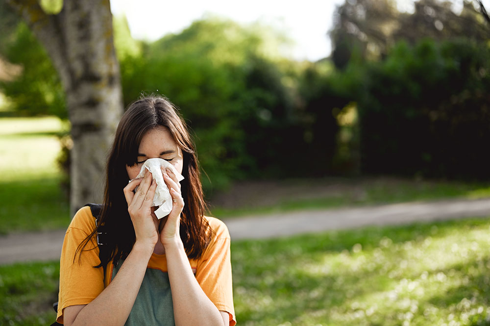 Pollen allergy patient sneezing into a tissue and seeking trusted allergy care in the Louisville and Florence, Kentucky area.